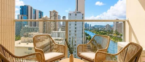 A balcony with wicker furniture, a round table, and a city view.
