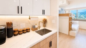 A modern kitchen with white cabinets, a stainless steel sink, and a built-in wooden bed with a city view. - Luxe Island Retreat – Modern Coastal Design (Honolulu)