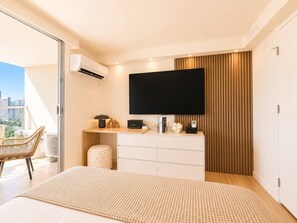 A modern bedroom with a bed, a flat-screen TV, a dresser, and a chair. - Luxe Island Retreat – Modern Coastal Design (Honolulu)