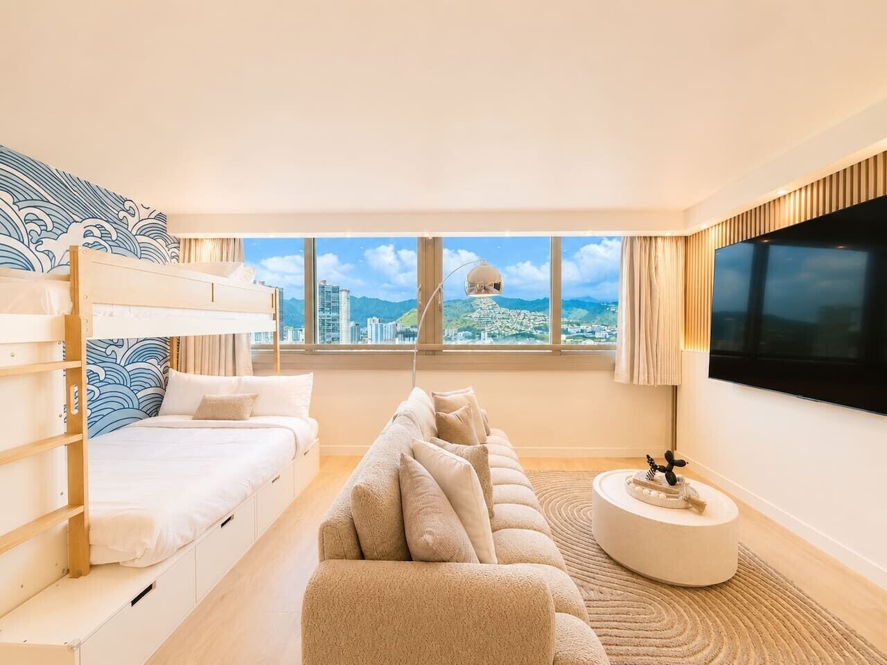 Een moderne hotelkamer met een stapelbed, een slaapbank, een ronde salontafel en een groot televisiescherm.