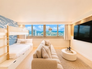 A modern hotel room with a bunk bed, a sofa, a round coffee table, and a large TV screen. - Luxe Island Retreat – Modern Coastal Design (Honolulu)