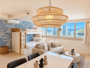 A modern room with a bunk bed, a sofa, a dining table, and a large window with a city view. - Luxe Island Retreat – Modern Coastal Design (Honolulu)