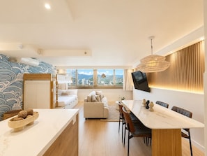 A modern living space with a dining area, a sofa, and a view of the cityscape. - Luxe Island Retreat – Modern Coastal Design (Honolulu)