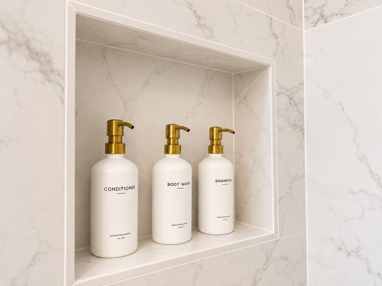 Une étagère de salle de bain avec trois flacons blancs contenant des produits de soins pour le corps.