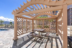 Eine hölzerne Pergola mit Tisch und Bänken, mit Blick auf einen Poolbereich.