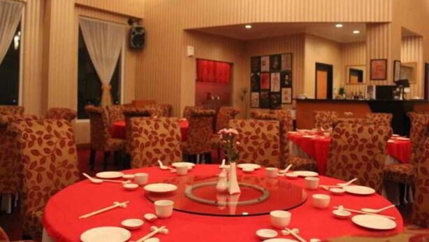 Un comedor con mesas redondas, sillas y manteles rojos.