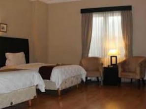 A hotel room with two beds, a chair, a nightstand, and a window with curtains. - Luminor Hotel Palembang (Palembang)