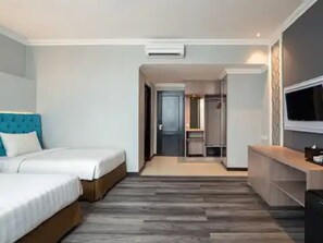 A hotel room with two beds, a wooden floor, a TV, and a wardrobe. - Luminor Hotel Palembang (Palembang)