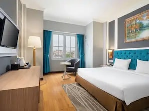 Ein Hotelzimmer mit Bett, Schreibtisch, Stuhl, Fernseher und einem Fenster mit Vorhängen.