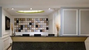 Un mostrador de recepción con un diseño en la pared de fondo, un espejo a la izquierda y dos jarrones con flores secas a la derecha.