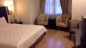 Ein Hotelzimmer mit einem Bett, zwei Sesseln, einem kleinen Tisch und einem Fernseher.