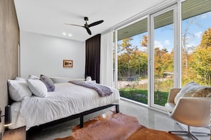 A modern bedroom with a bed, a ceiling fan, a large window, and a view of the outdoors. - Ultra Luxury Chalet: Private Oasis, Spa, Sauna (Les Laurentides Regional County Municipality)