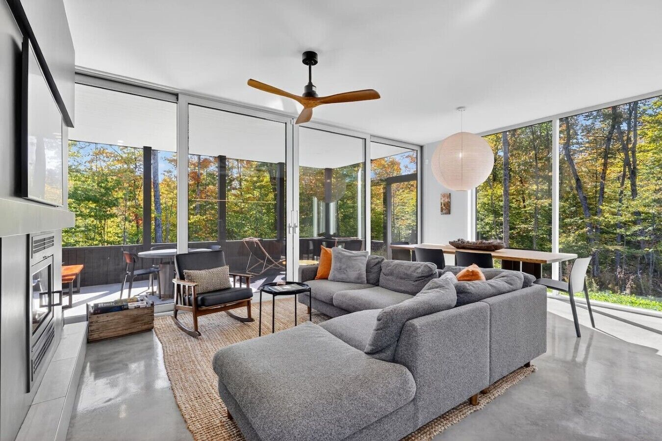 Ein modernes Wohnzimmer mit einem großen, grauen Ecksofa, einem Esstisch und einem Deckenventilator.