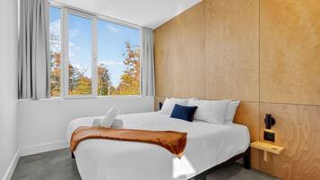 Une chambre d’hôtel avec un grand lit, une tête de lit en bois, une fenêtre avec des rideaux et une table de chevet avec une lampe.