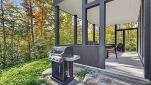 Eine moderne Terrassengrundstueck mit integriertem Grill, umgeben von einem Holzboden und Blick auf herbstliche Laubfärbung.