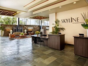 A reception area with a reception desk, seating, and a wall with the name 'SKYLINE AT ISLAND COLONY'. - 41F Modern Waikiki Retreat – Luxe Coastal Style (Honolulu)