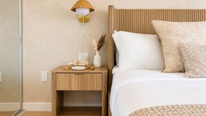 Een slaapkamer met een houten nachtkastje, een bedlampje, een bed met witte beddengoed en een getextureerd vloerkleed.