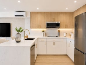 A modern kitchen with white cabinetry, stainless steel appliances, and a marble countertop. - Waikiki Ocean Breeze Escape: Coastal Luxe (Honolulu)