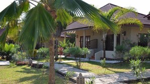 Um imóvel residencial com telhado de cerâmica, um jardim bem cuidado com palmeiras, e um caminho que leva à entrada.