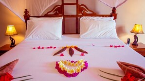 Uma cama com dossel, duas luminárias de cabeceira e um arranjo floral decorativo sobre o lençol.