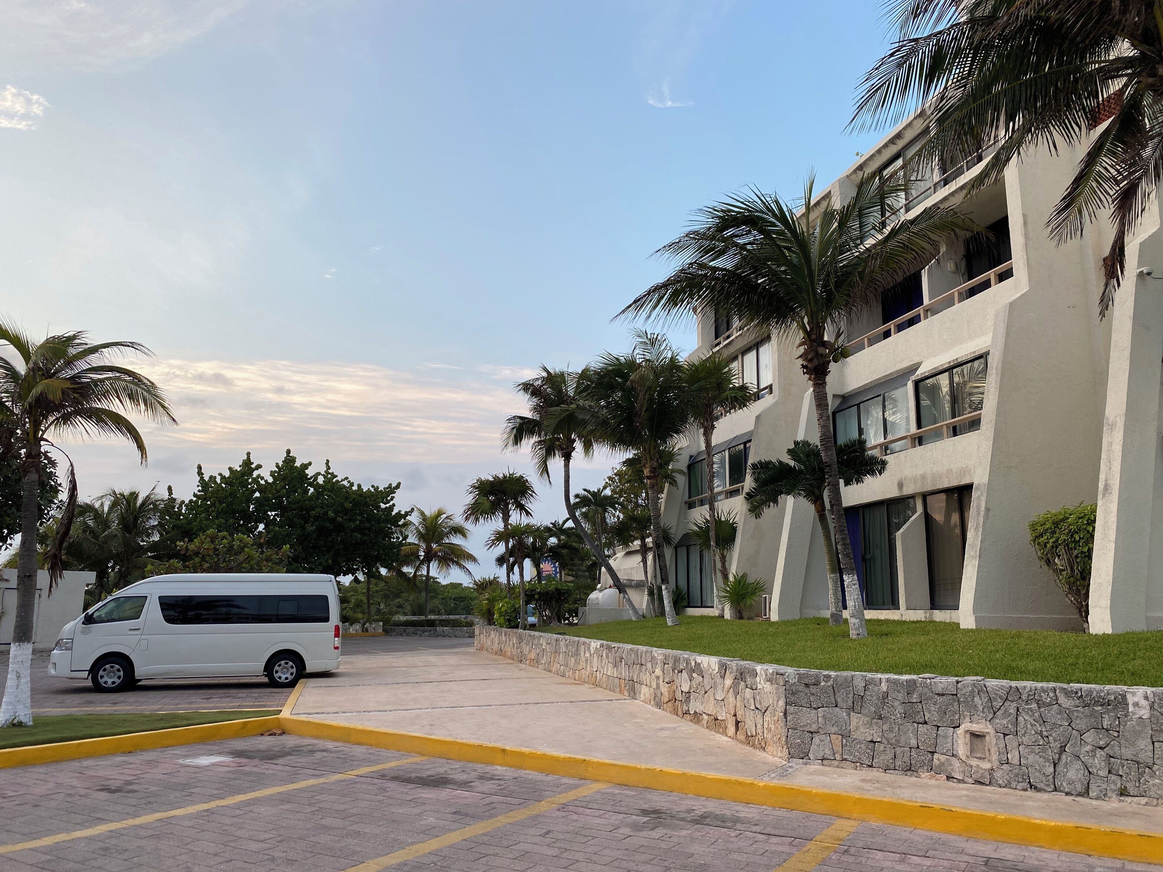 A modern building with a parking area, palm trees, and a white van.