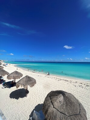 Ein Strand mit weißem Sand, klarem türkisblauem Wasser und Reetdachschirmen.