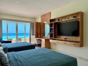 A hotel room with two beds, a TV, a desk, and a large window overlooking the ocean. - Five Bedroom Beachfront Villa - Private Heated Pool & Beach Access (Cancun)