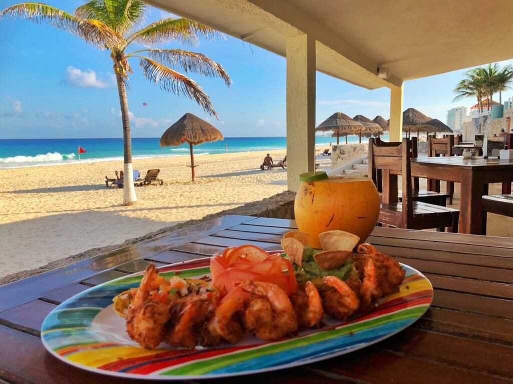 A beachside dining area with a plate of shrimp and a coconut on a table.