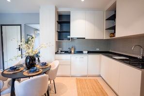 A modern kitchen with white cabinets, a black countertop, and a dining area with a table set for two. - The Title Legendary 2BR Pool Access, Bang Tao, Phuket (Choeng Thale)