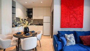 A modern living space with a dining area, kitchen, and a blue sofa with a red accent wall. - The Title Legendary 2BR Pool Access, Bang Tao, Phuket (Tambon Choeng Thale)