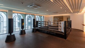 A boxing ring with a padded floor, surrounded by large windows with arched tops, and a ceiling with linear lighting. - The Title Legendary 2BR Pool Access, Bang Tao, Phuket (Tambon Choeng Thale)
