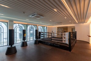 Ein Boxring mit gepolstertem Boden, umgeben von großen Fenstern mit Rundbögen, und einer Decke mit linearer Beleuchtung.
