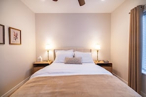 Ein Hotelzimmer mit einem großen Bett, zwei Nachttischen, einem Deckenventilator und einem mit Vorhängen versehenen Fenster.