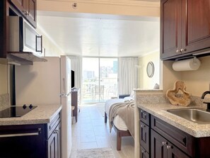 A compact kitchen with a microwave, stove, and sink. There is a balcony with a view of the city. - Tropical Breeze Getaway – Comfort & Charm (Honolulu)