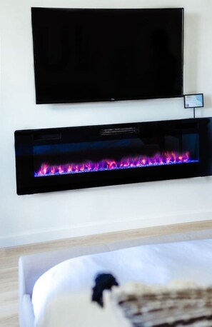 A room with a flat-screen TV mounted on the wall above a fireplace with a visible fire. - Ocean View Across Waikiki Beach Modern Bungalow (Honolulu)
