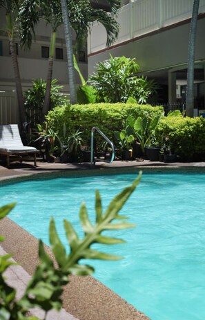 A swimming pool with a clear blue water, surrounded by lush green plants and palm trees. - Ocean View Across Waikiki Beach Modern Bungalow (Honolulu)
