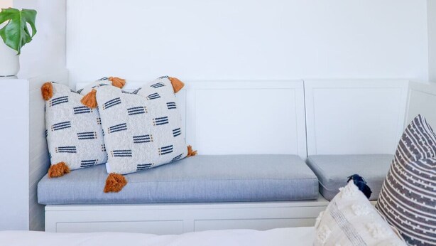 Een bed met witte beddengoed, een grijze bank met gestreepte kussens, en een gestreept kussen.