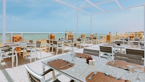 An outdoor dining area with tables and chairs, overlooking a beach and the sea. - Pickalbatros Portofino Villaggio Resort (Marsa Alam)