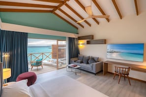 A hotel room with a bed, a sofa, a desk, and a chair. There is a balcony with a view of the sea.