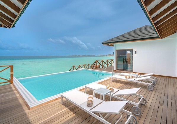 Un espace aménagé au bord de la piscine, avec des chaises longues, une terrasse en bois et une vue sur l’océan.