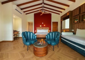 A hotel room with a bed, two blue armchairs, a wooden coffee table, and a red accent wall.