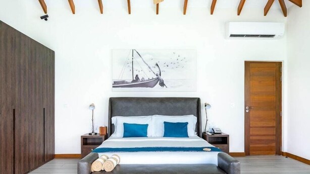 A bedroom with a bed, a painting, a wooden door, and an air conditioning unit.