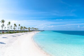 A beach with white sand, clear turquoise water, and palm trees.