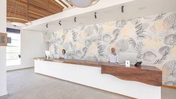 A reception area with a wooden reception desk, a white wall with a leaf pattern, and a ceiling with wooden beams and hanging lights.