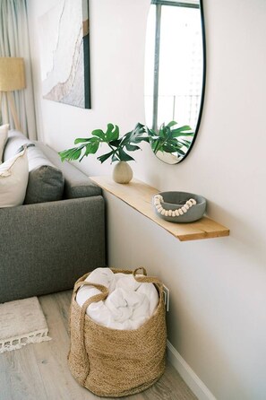 A modern living room with a grey sofa, a wooden shelf with a plant and a bowl, a woven basket, and a large mirror on the wall. - Waikiki Gem, Stunning Ocean View, Parking Included (Honolulu)