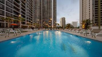 A swimming pool with lounge chairs and a high-rise building in the background.