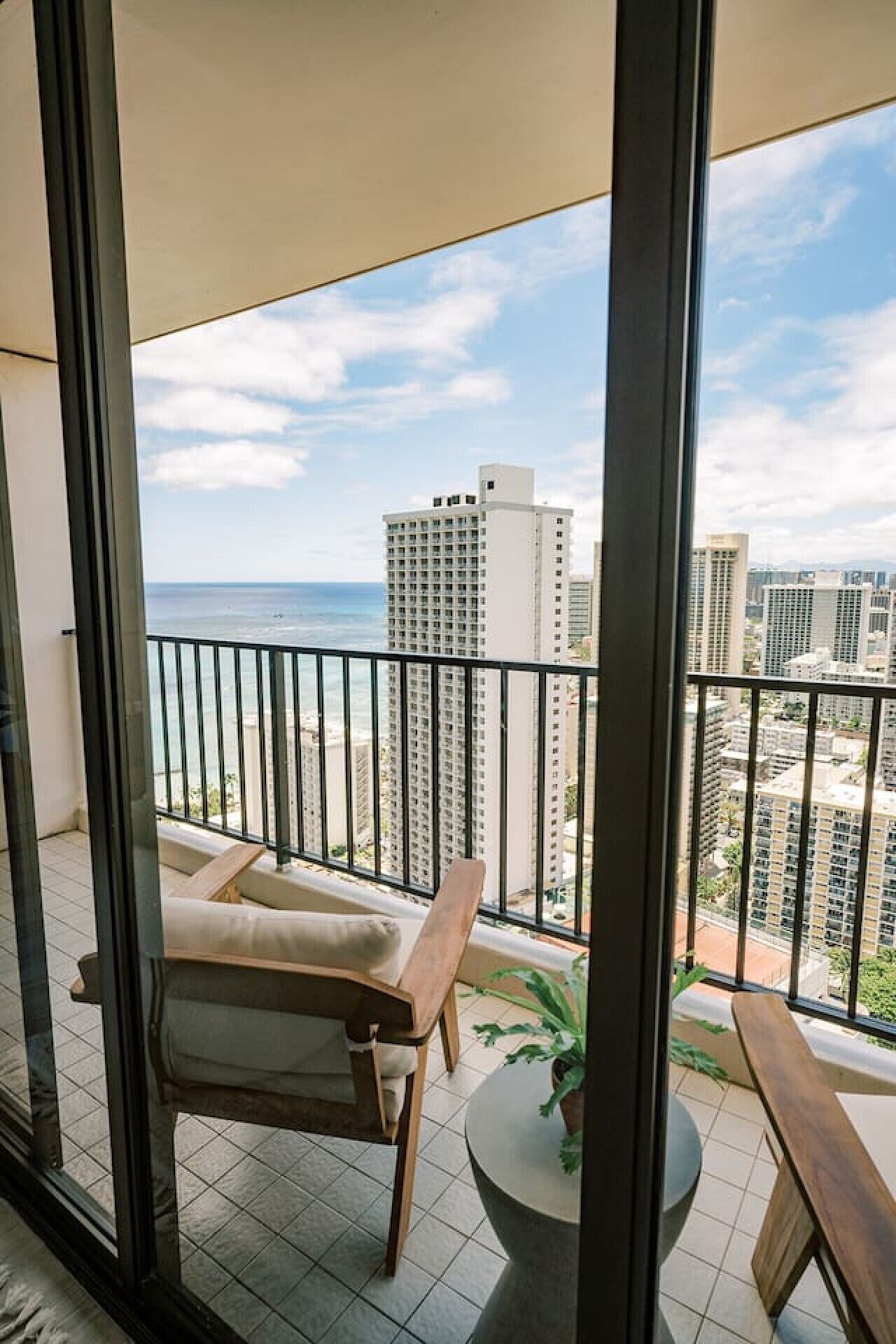 Ein Balkon mit Blick auf das Meer und die Stadtlandschaft, ein Stuhl, ein kleiner Tisch und ein Blumentopf.