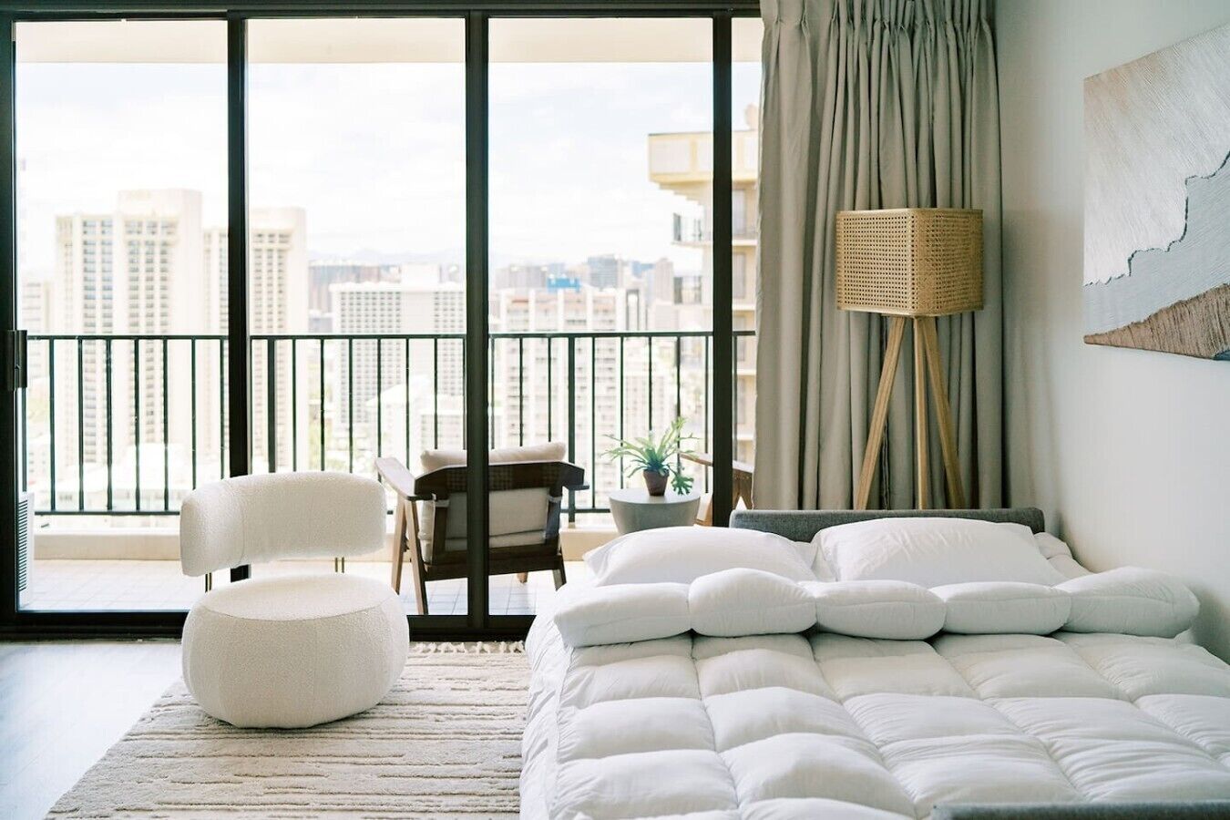 Una camera da letto con un letto grande, una sedia, un tavolino con una pianta e vista sulla città da un balcone.