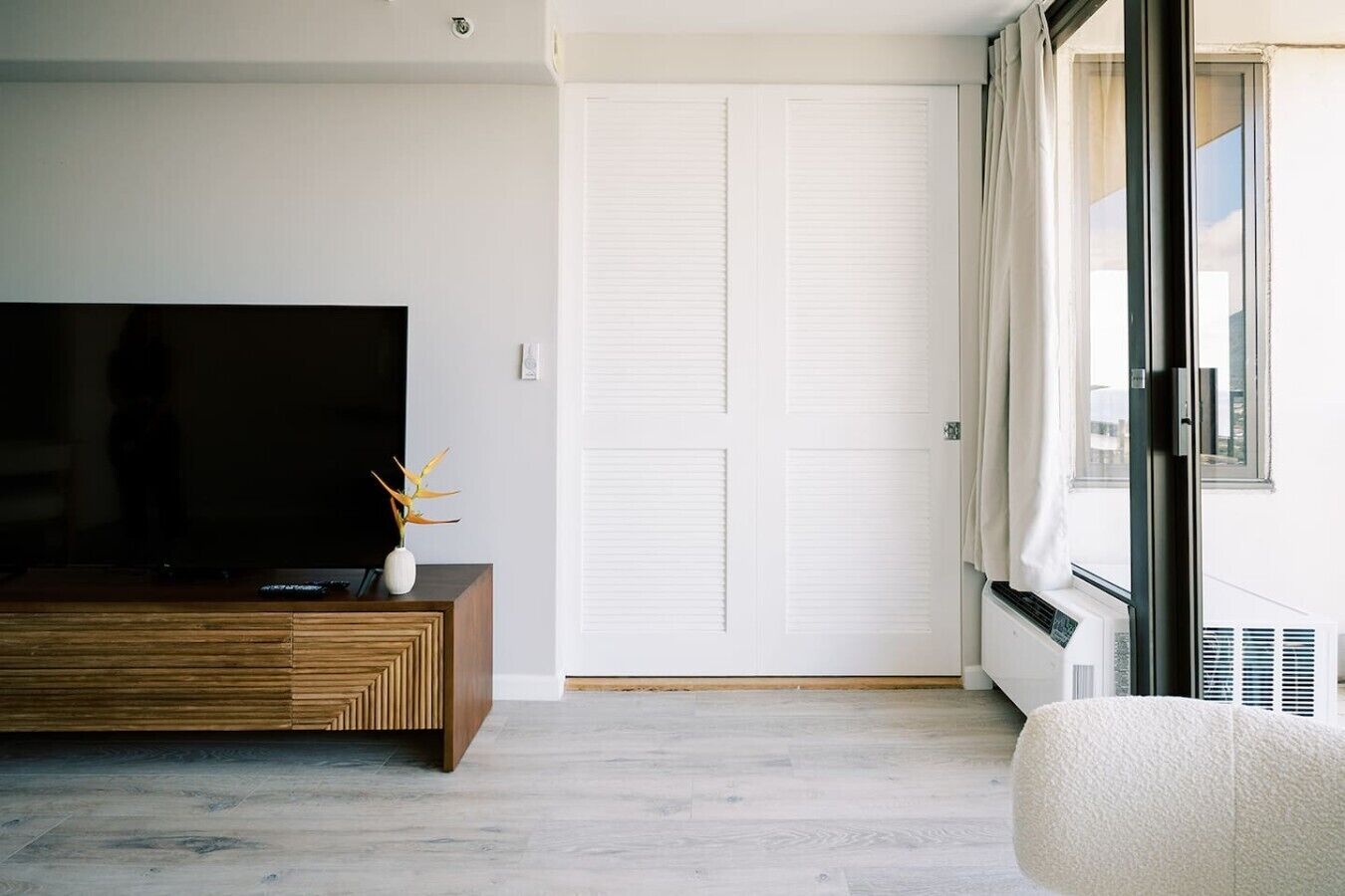 Un salon moderne avec un téléviseur à écran plat, un meuble en bois et un canapé blanc.