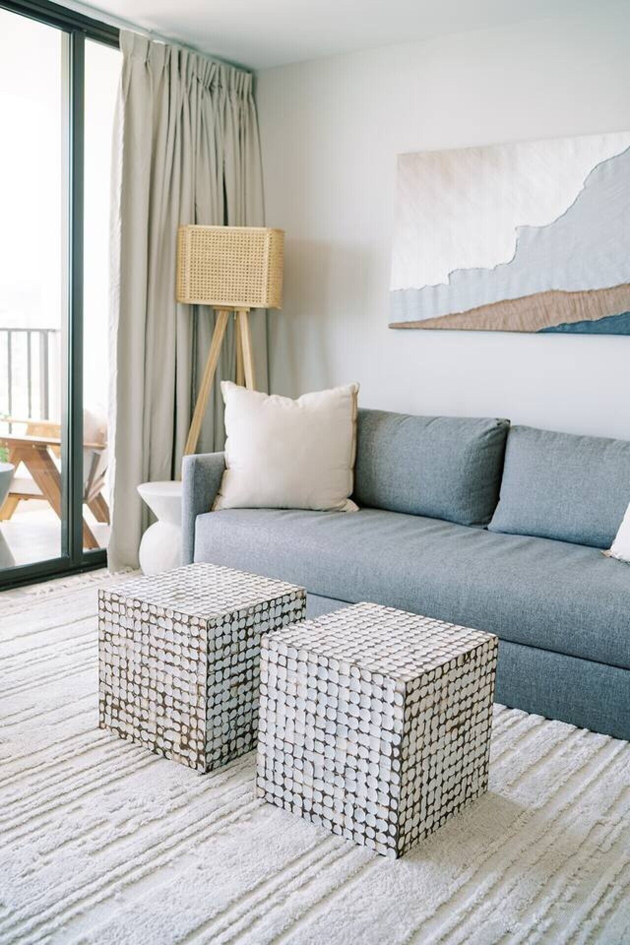 Un soggiorno moderno con un divano grigio, due pouf decorati, un tavolino bianco e una sedia in rattan.